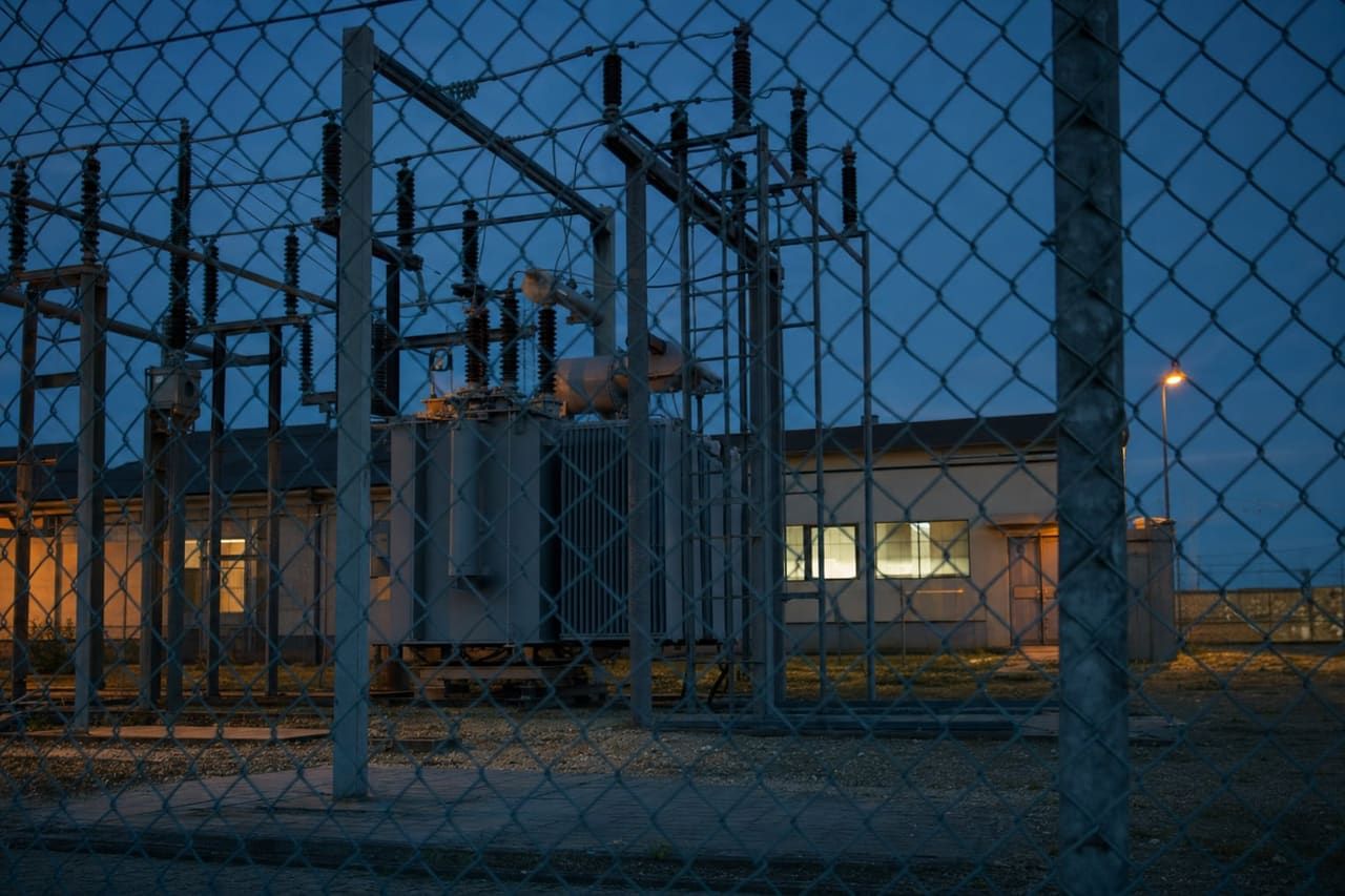 Umspannwerk in der blauen Stunde hinter einem Maschendrahtzaun