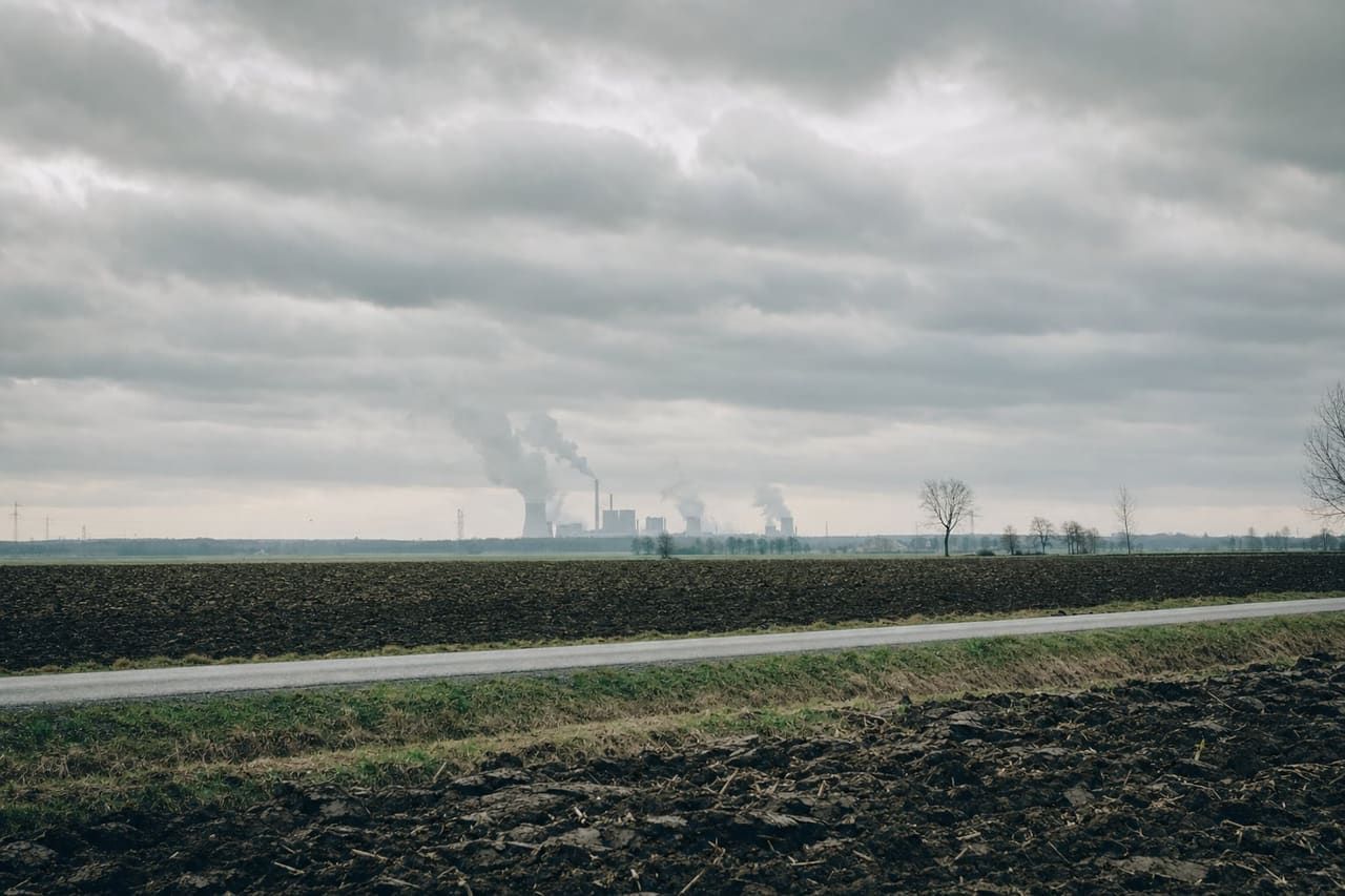 Weite Landschaft unter schwerem Himmel, am Horizont eine Industrieanlage