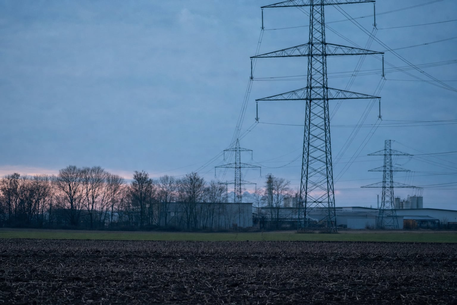 Hochspannungsmasten über flacher Agrarlandschaft in der Dämmerung